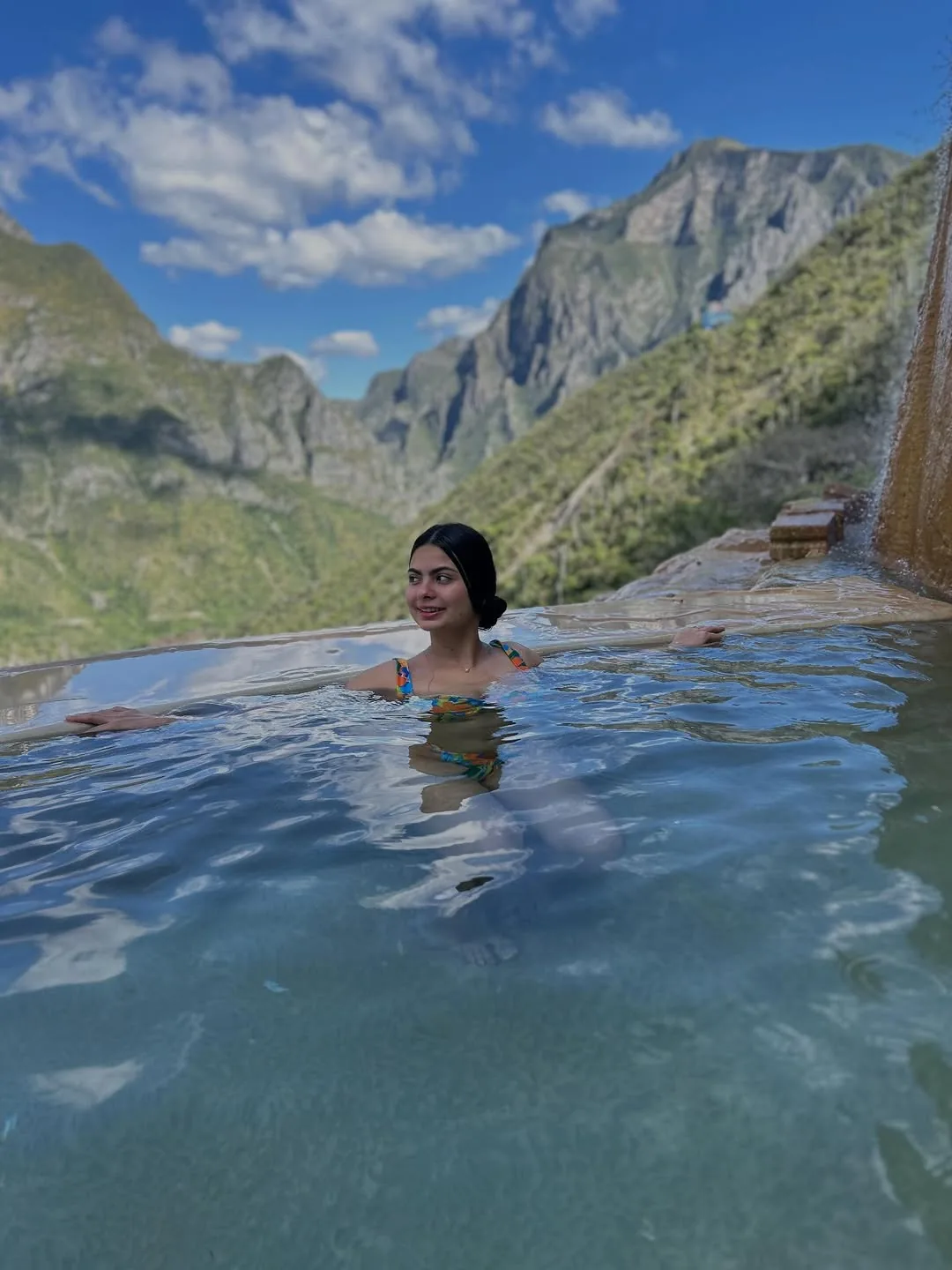 Mujer en la poza infinita con vista a las montañas